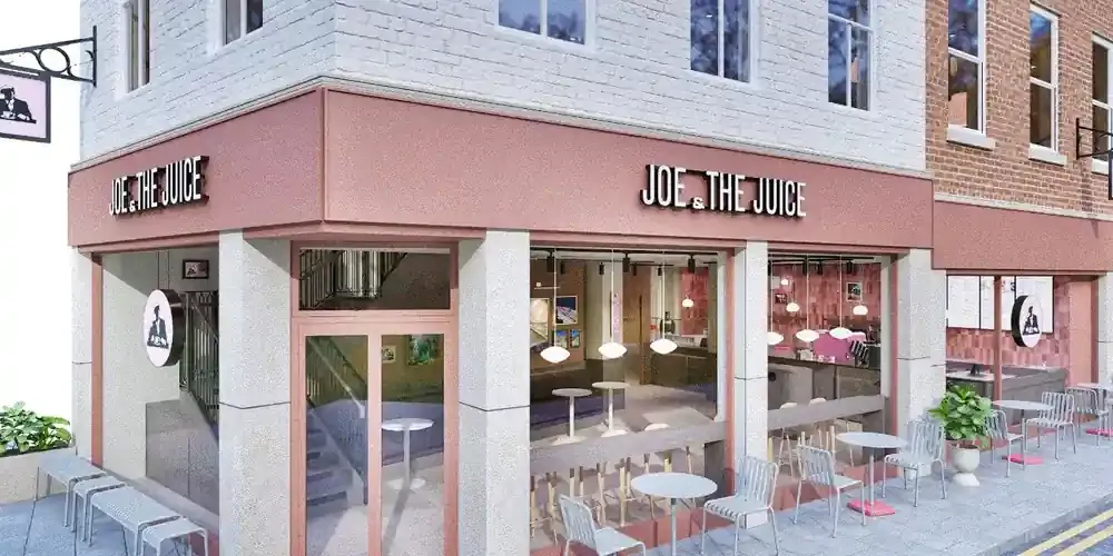 Architect's visual of the proposed Joe & The Juice store on the corner of Feasegate and St Sampson's Square, York: a painted brick building with a pink fascia and lettering to both frontages, full height glazing with window bar seating, and café tables and chairs on the pavement.