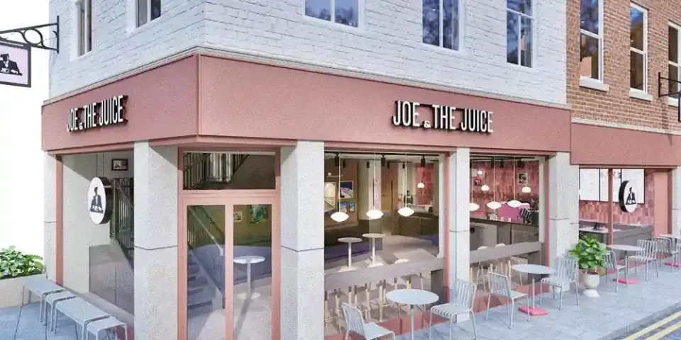 Architect's visual of the proposed Joe & The Juice store on the corner of Feasegate and St Sampson's Square, York: a painted brick building with a pink fascia and lettering to both frontages, full height glazing with window bar seating, and café tables and chairs on the pavement.