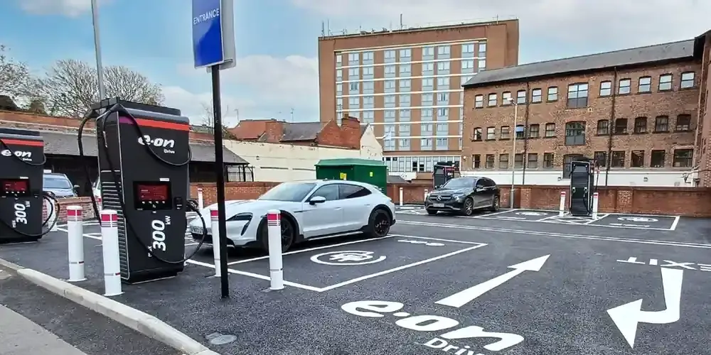 The E.ON Drive EV charging hub off North Street, York. Two E.ON Drive ultra-rapid chargers stand in the foreground, a white electric car is parked on a charging bay marked with the E.ON Drive logo, and brick office buildings line the far side of the car park.